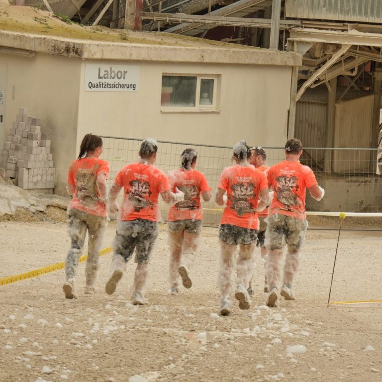 Fünf Personen in orangefarbener Kleidung joggen über einen staubigen Untergrund.